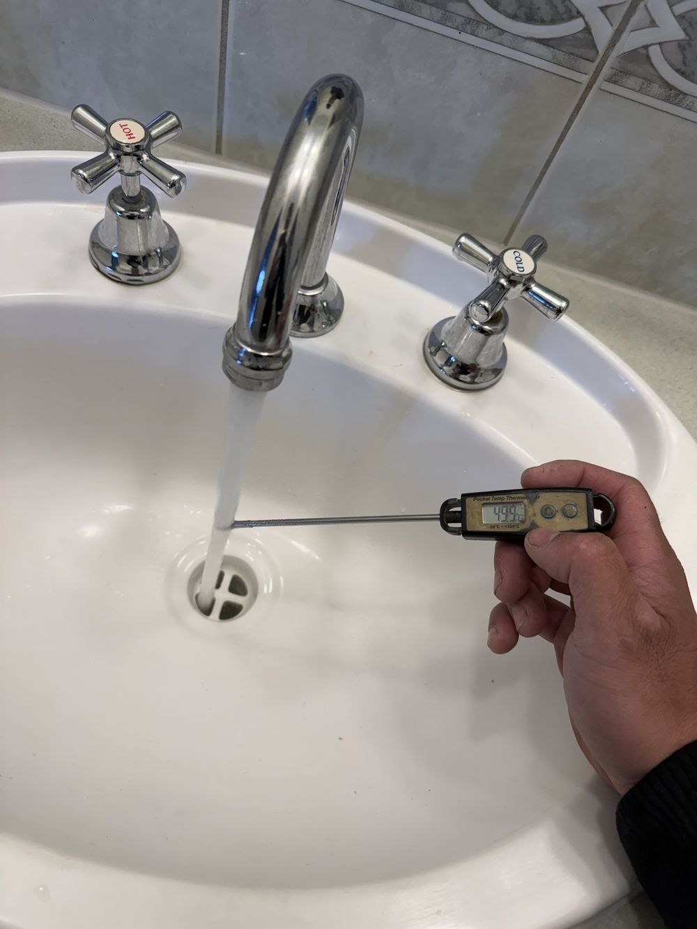 Thermometer measuring 49.9 degrees Celsius hot water from a basin tap after tempering valve replacement in Wantirna South