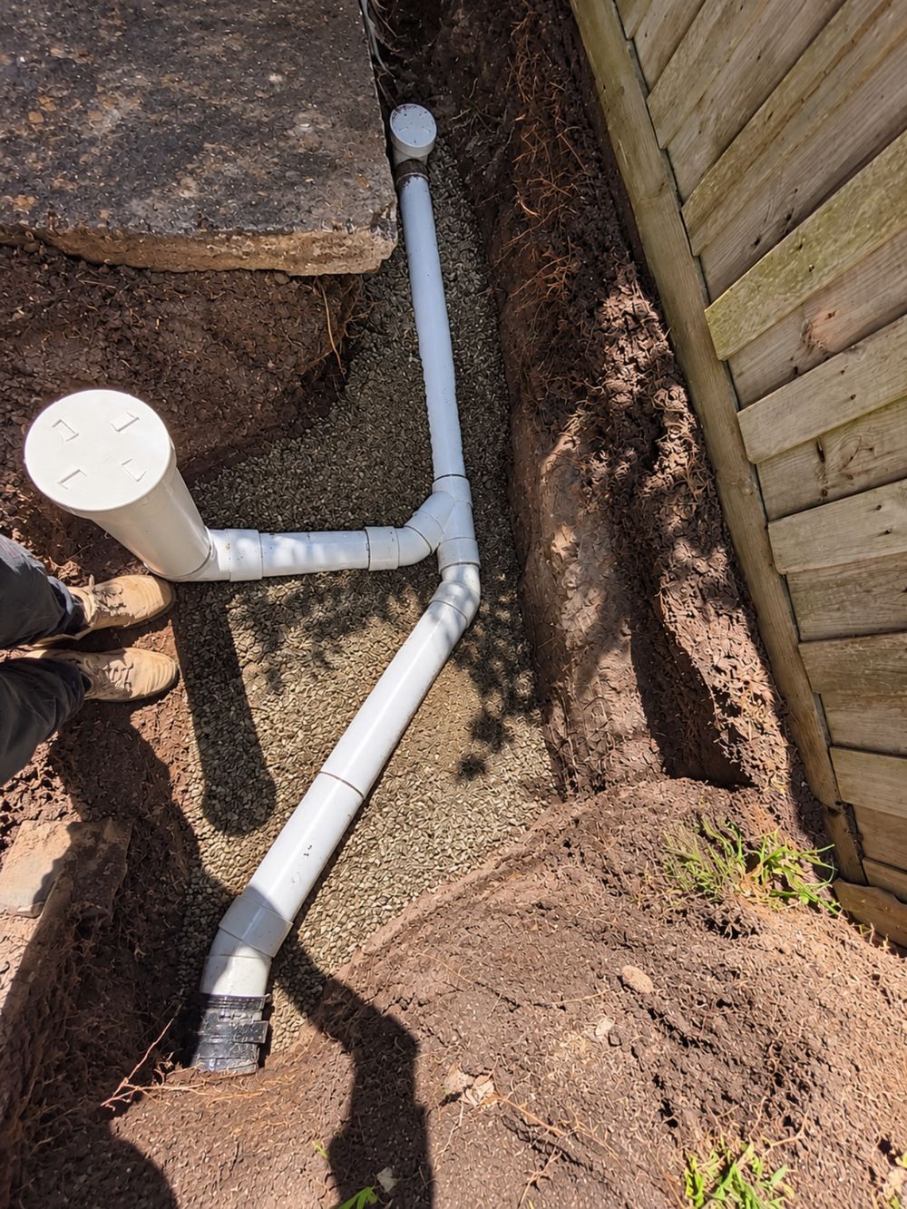 New white PVC stormwater drainage pipework laid in a gravel-bedded trench beside a timber fence in Scoresby